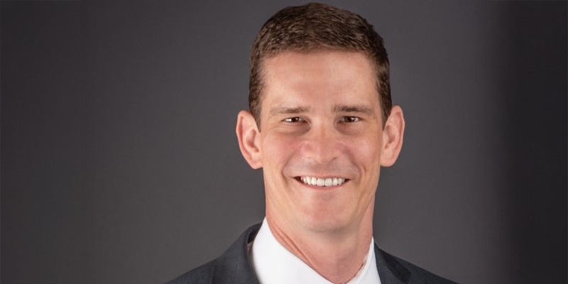 A smiling man in a suit posing for a professional headshot against a dark background